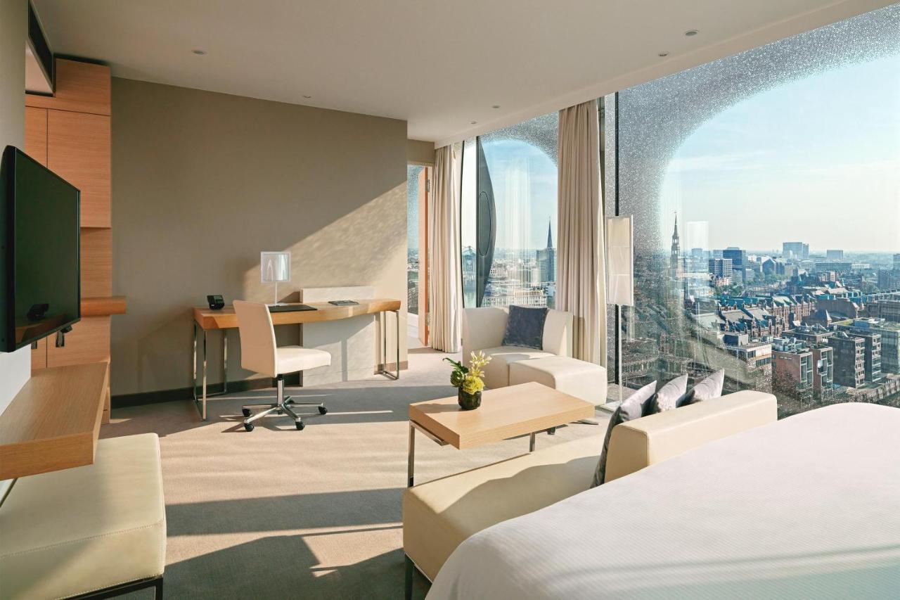 The Westin Hamburg Elbphilharmonie Hotel Luaran gambar The photo depicts a modern hotel room featuring a contemporary design. The space includes a large window that offers a panoramic view of the city beyond. Inside, there are stylish furniture elements such as a small dining table and chairs, a desk wit