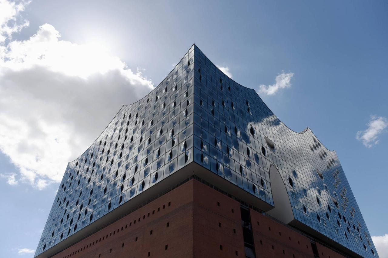 The Westin Hamburg Elbphilharmonie Hotel Luaran gambar The photo shows a modern architectural building characterized by a distinctive, wavy glass facade. The structure has a bluish tint with many large windows that reflect the sky and surrounding environment. The lower section of the building is made of 