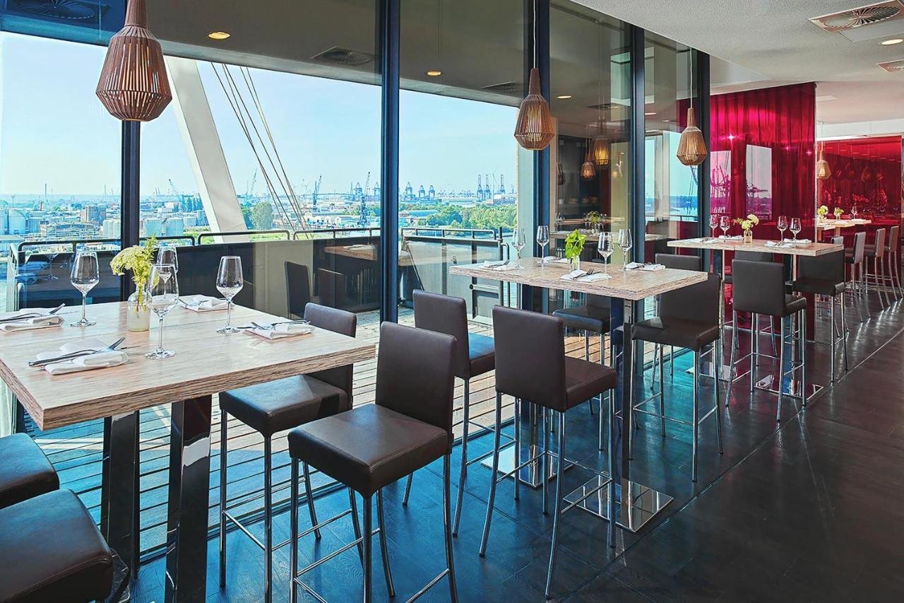 The Westin Hamburg Elbphilharmonie Hotel Luaran gambar The photo depicts a modern restaurant interior featuring a spacious dining area with large windows that provide a view of the outside. There are several tall tables with a light-colored surface and metallic bases, accompanied by dark, sleek stools. T