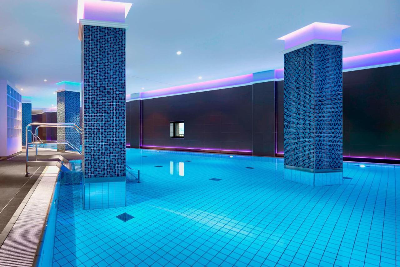 The Westin Hamburg Elbphilharmonie Hotel Luaran gambar The image shows a swimming pool area that features a modern, upscale design. The pool has bright blue tiles reflecting the water, creating a vibrant atmosphere. There are two columns dressed in a similar blue tile pattern, and the walls are adorned w
