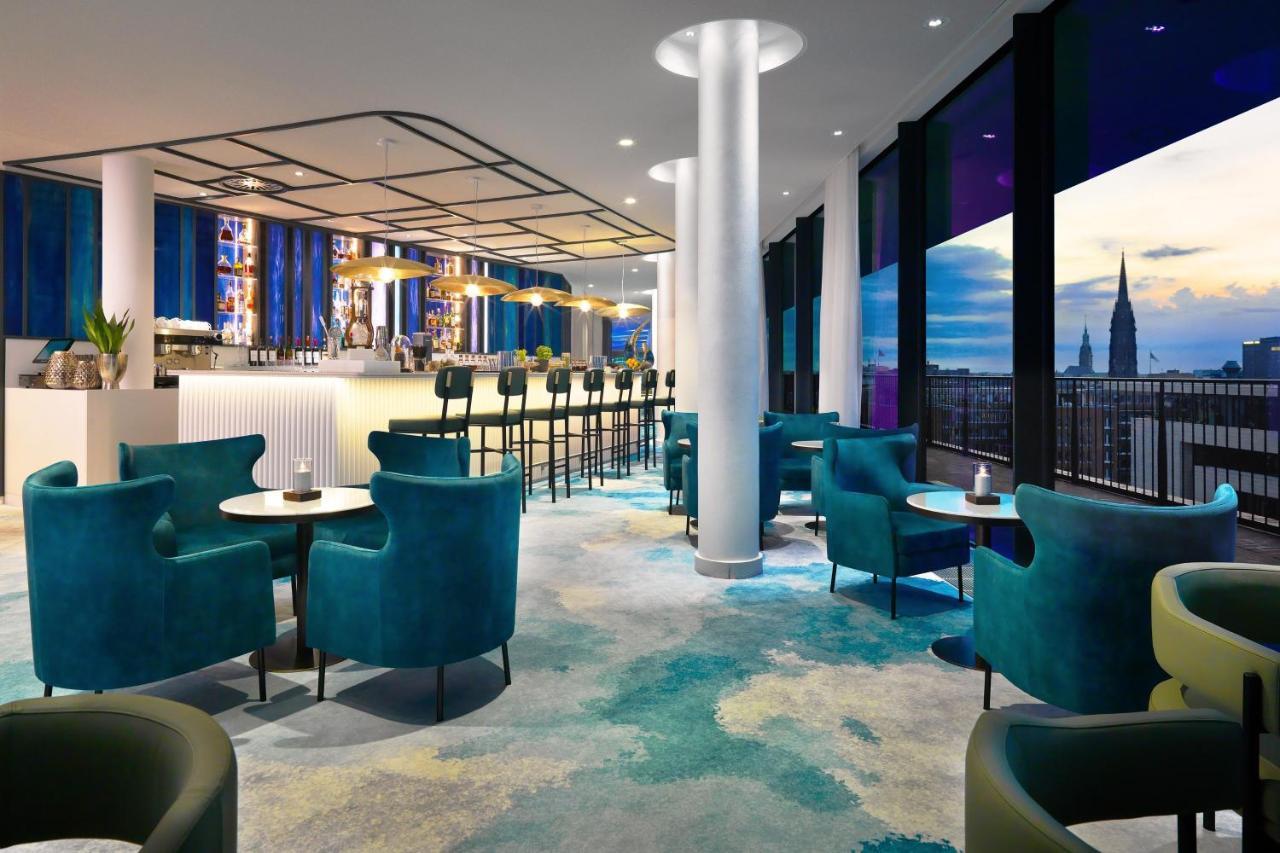 The Westin Hamburg Elbphilharmonie Hotel Luaran gambar The photo shows a modern lounge or bar area with a stylish design. It features plush turquoise chairs and small tables arranged around the space. In the background, there's a long bar with seating, illuminated by soft lighting. Large windows provide 
