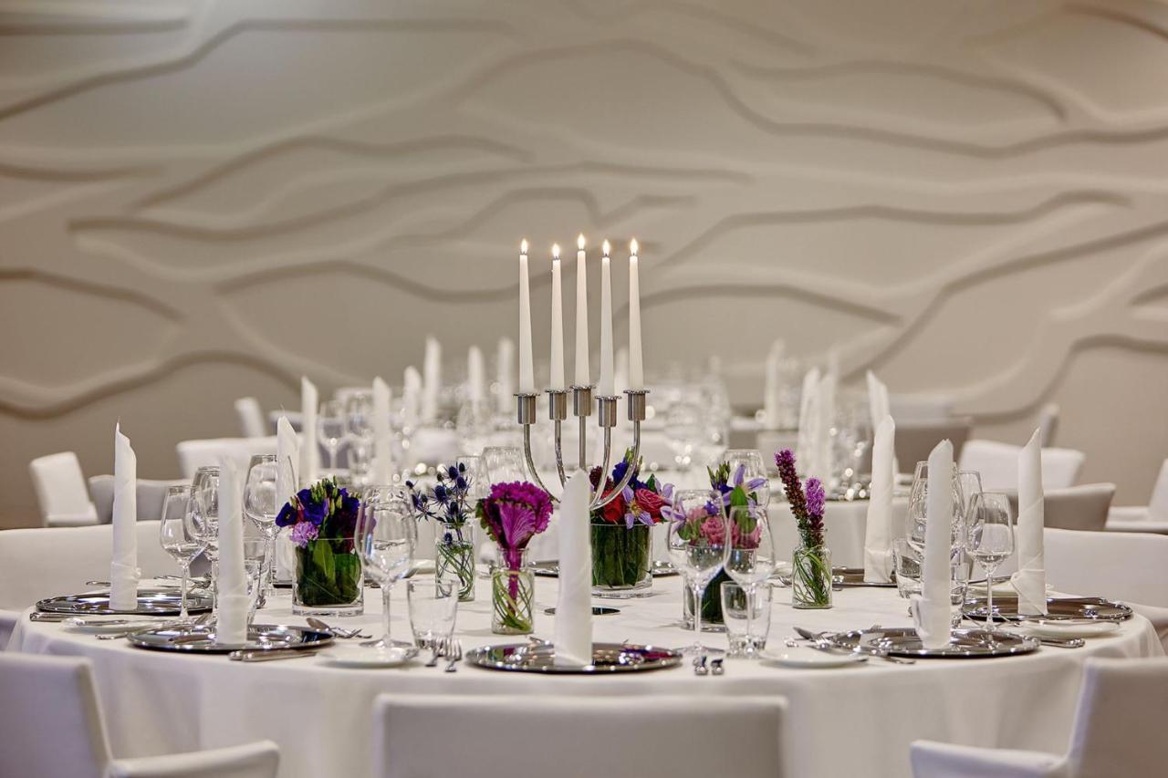 The Westin Hamburg Elbphilharmonie Hotel Luaran gambar The photo depicts an elegantly set round dining table. In the center, there is a candelabra with several tall candles, providing a soft, warm light. Surrounding the candelabra are small glass vases filled with colorful flowers, adding a vibrant touch
