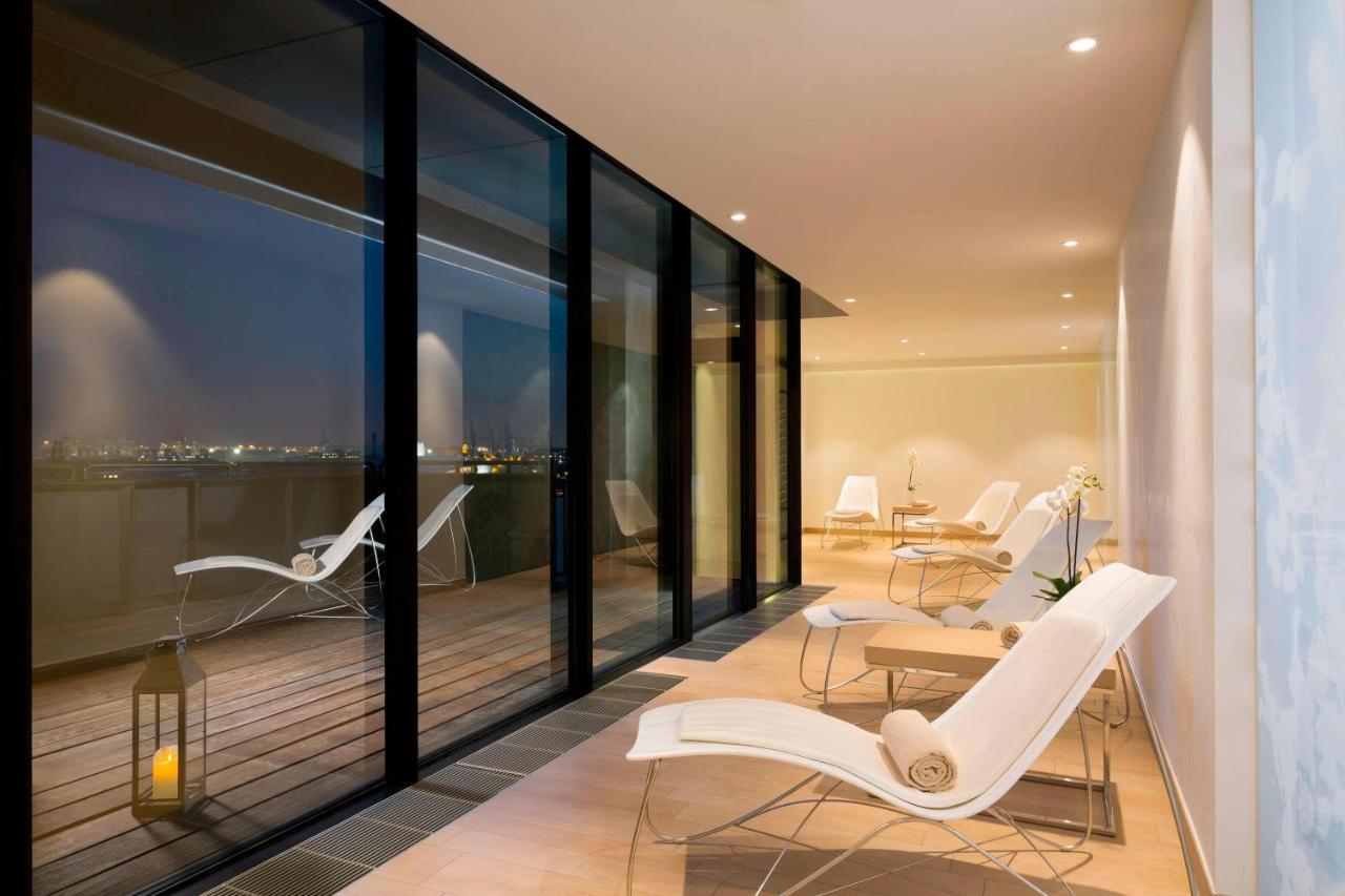 The Westin Hamburg Elbphilharmonie Hotel Luaran gambar The photo shows a modern, stylish indoor space with large glass windows that offer a view of the night. The area is illuminated softly, highlighting a sleek and minimalist design. There are several white lounge chairs arranged on a wooden deck, creat
