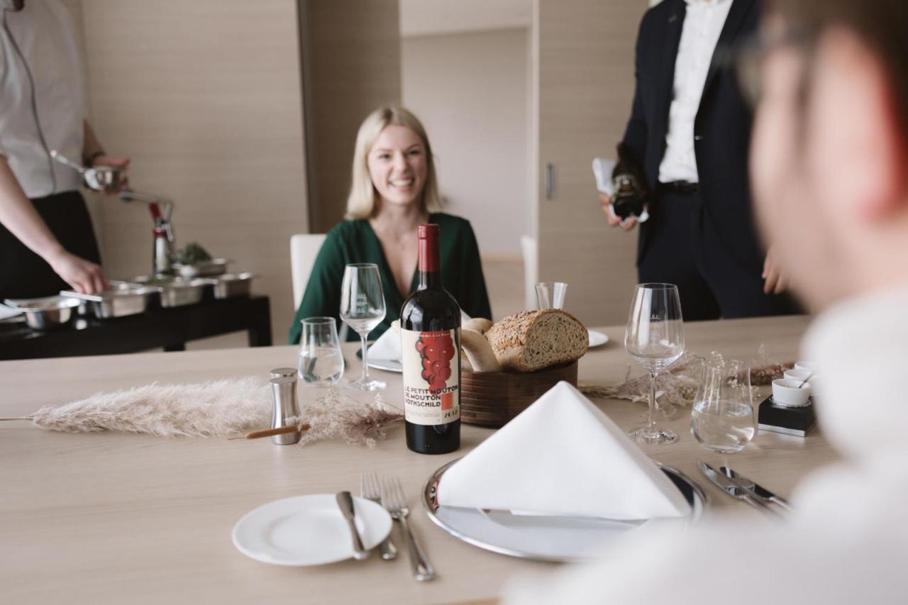 The Westin Hamburg Elbphilharmonie Hotel Luaran gambar The image shows a dining setting with a woman smiling at the table. She is seated in front of a bottle of red wine that has a distinctive label. There is also bread and a neatly arranged table setting, including plates and glasses. In the background,