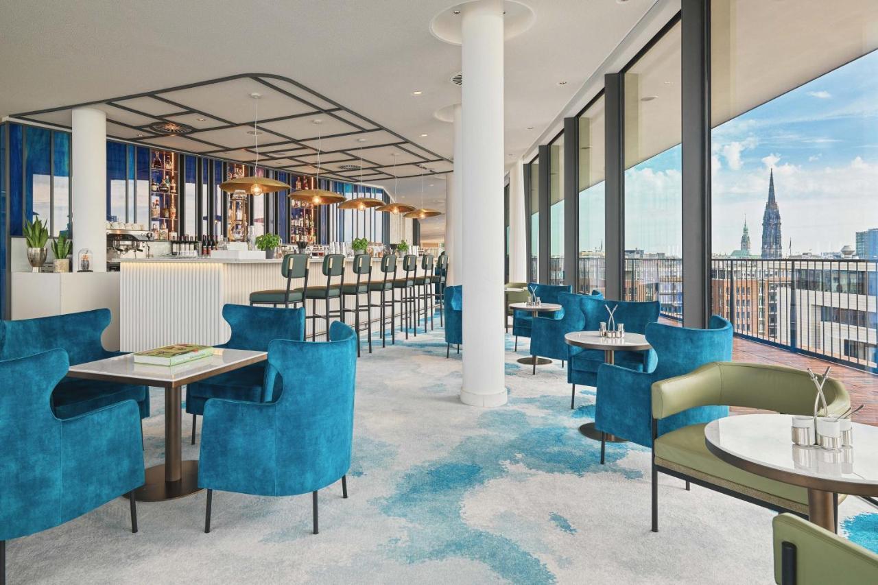 The Westin Hamburg Elbphilharmonie Hotel Luaran gambar The image shows a stylish and modern restaurant interior. There are several tables with blue and green chairs, creating a cozy atmosphere. The flooring features a light carpet with abstract patterns. Large windows provide plenty of natural light and 
