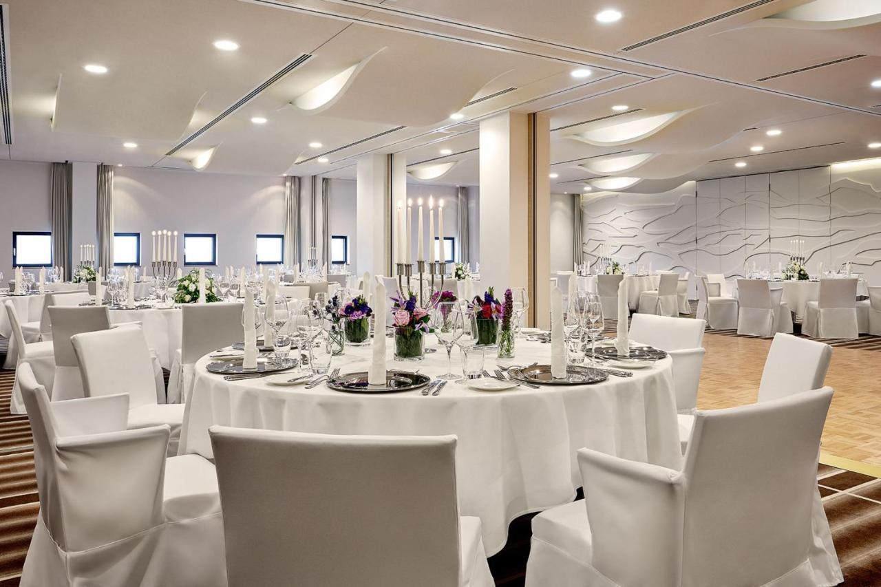 The Westin Hamburg Elbphilharmonie Hotel Luaran gambar The photo depicts a modern banquet or event hall setup. It features round tables covered with white tablecloths, each set with elegant dishware and glassware. The tables are adorned with floral centerpieces, adding a touch of color, and there are tal