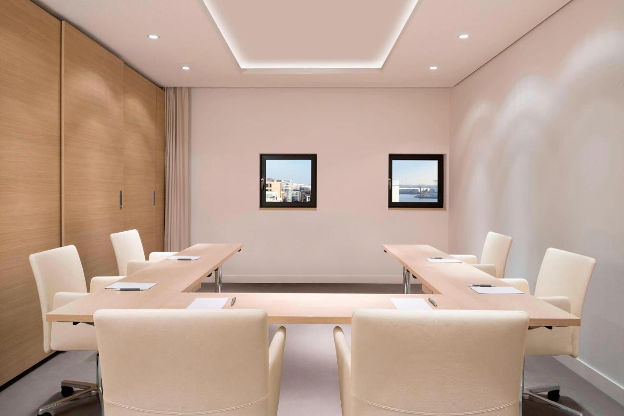 The Westin Hamburg Elbphilharmonie Hotel Luaran gambar The photo shows a modern conference room. It features a long, rectangular table made of light-colored wood, surrounded by several cream-colored chairs. The walls are painted in a light shade, and there are two framed windows on one wall that provide 