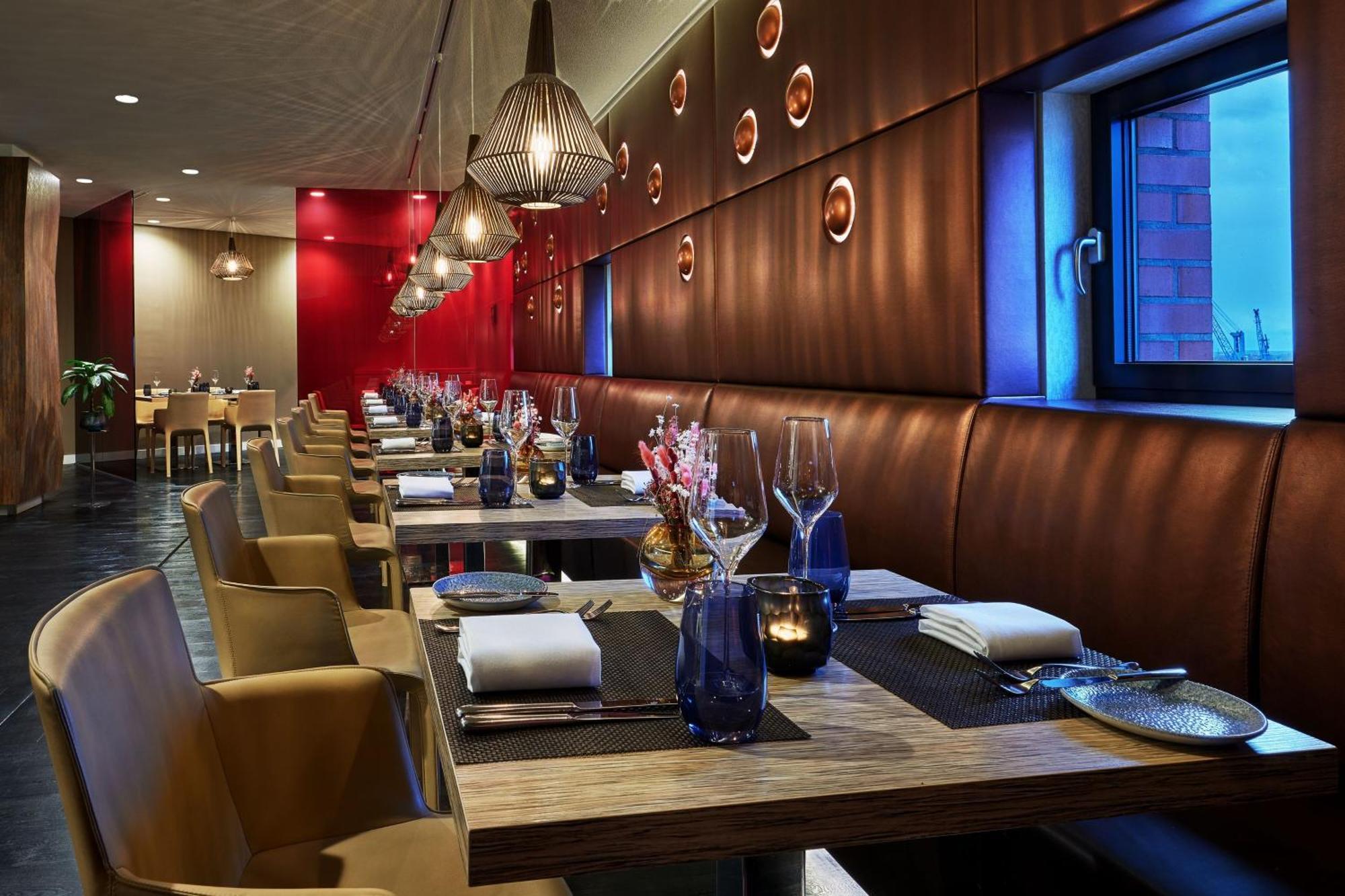 The Westin Hamburg Elbphilharmonie Hotel Luaran gambar The photo shows a modern restaurant interior. It features a series of wooden tables set for dining, each equipped with white napkins and utensils. The seating consists of comfortable leather chairs. The walls are decorated with a combination of warm 
