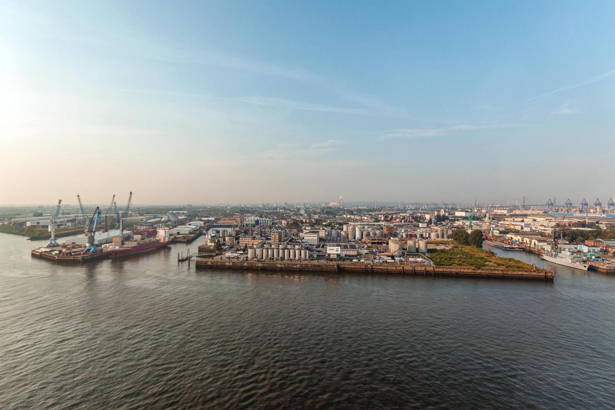 The Westin Hamburg Elbphilharmonie Hotel Luaran gambar The photo shows a coastal area with a large body of water in the foreground. To the left, there are industrial structures like cranes and cargo ships, indicating an active port or shipping area. In the background, there are various buildings, which a
